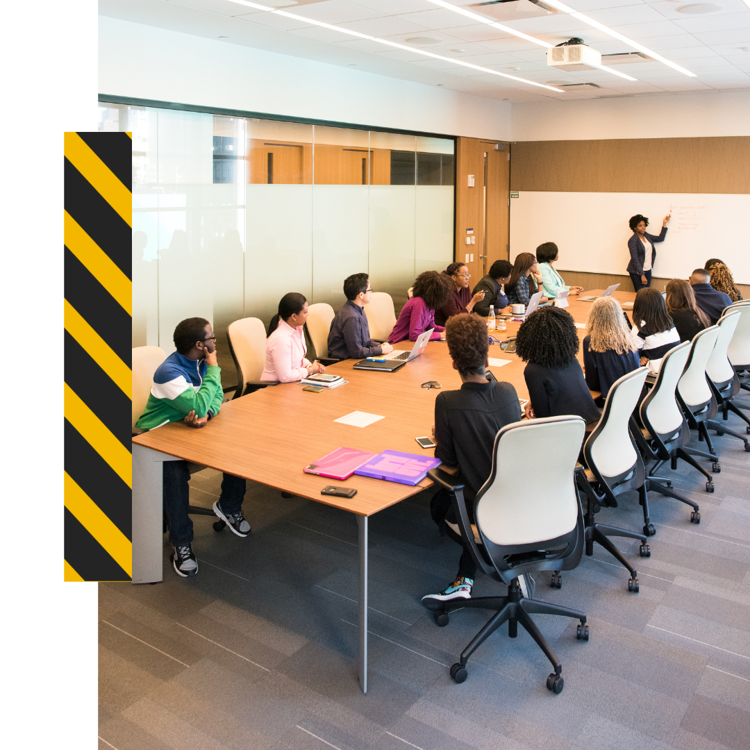 conference room full of people sitting at a long table with a presenter at the head